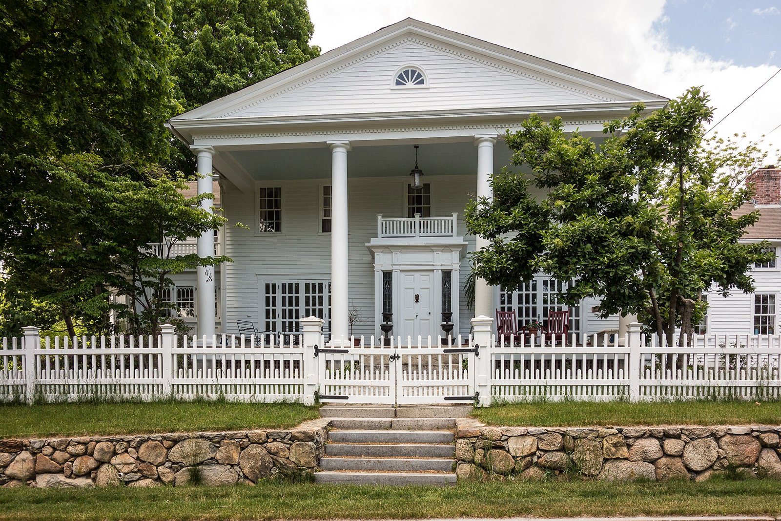 Greek Revival home with white picket fence and stone wall in West Warwick, Rhode Island